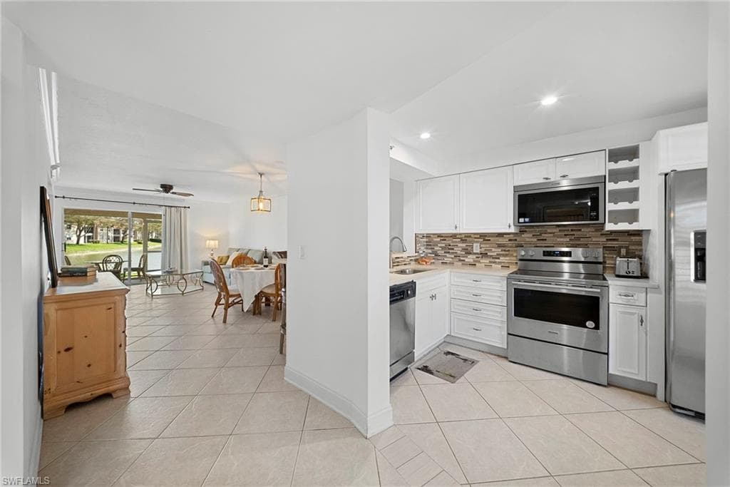 Kitchen featuring stainless steel appliances, white cabinetry, light tile patterned floors, backsplash, and open floor plan