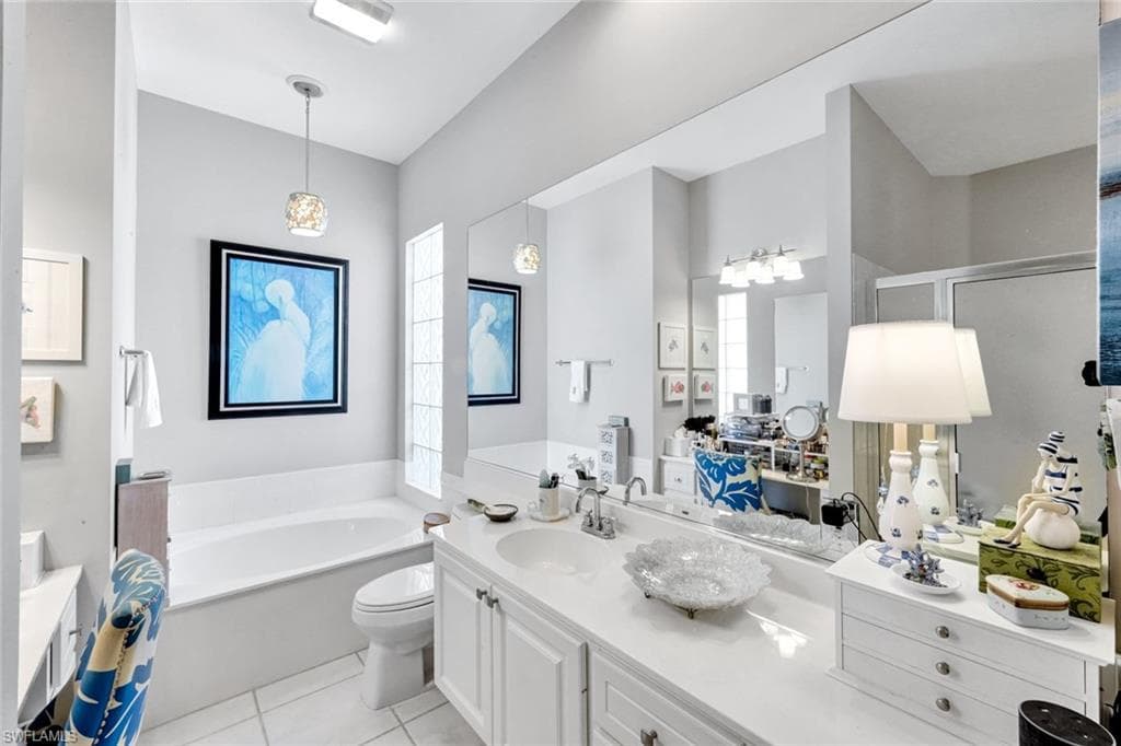 Bathroom featuring a built-in tub, dual sink vanity with white cabinetry, glass block window, and tile flooring