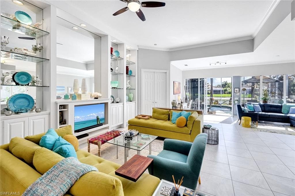 Spacious living area featuring tile flooring, built-in cabinetry with glass shelving, and a ceiling fan