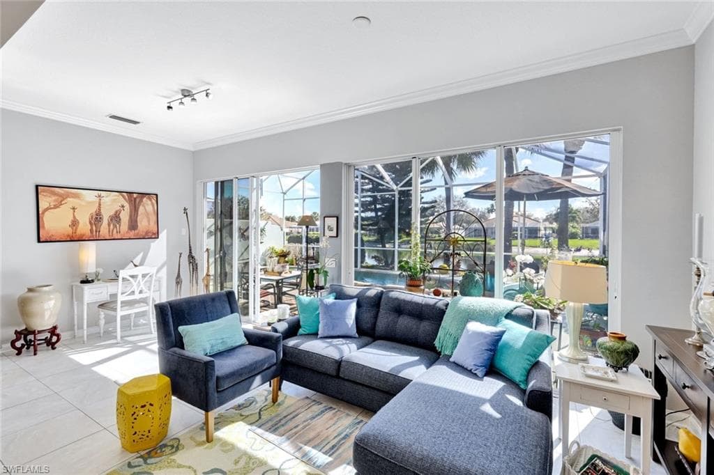 Spacious living area featuring large format tile flooring, crown molding, and sliding glass doors opening to a screened lanai and pool area
