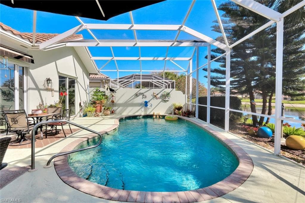 Screen-enclosed pool area featuring a freeform pool with a handrail, paver coping, and a concrete deck