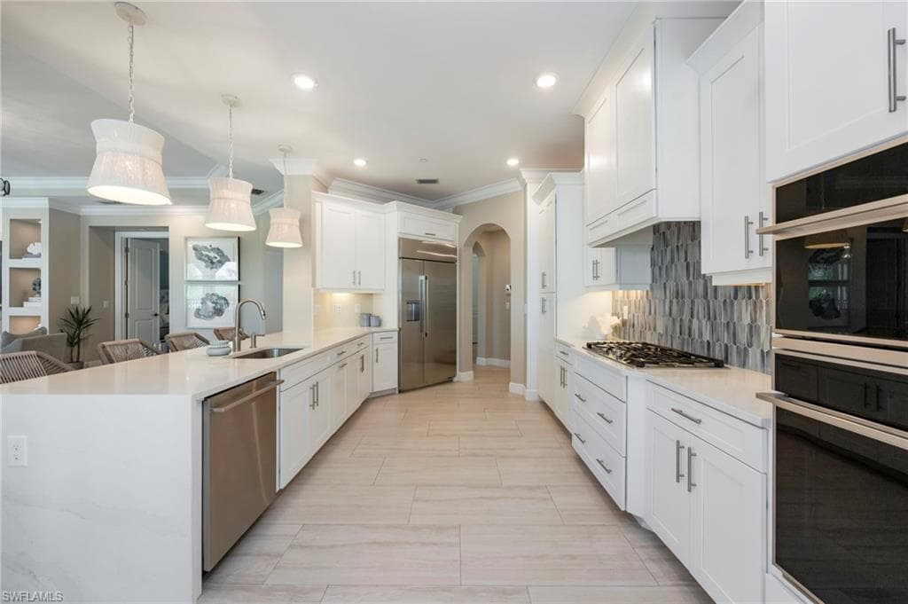 Kitchen featuring arched walkways, light stone counters, stainless steel appliances, a peninsula, and ornamental molding