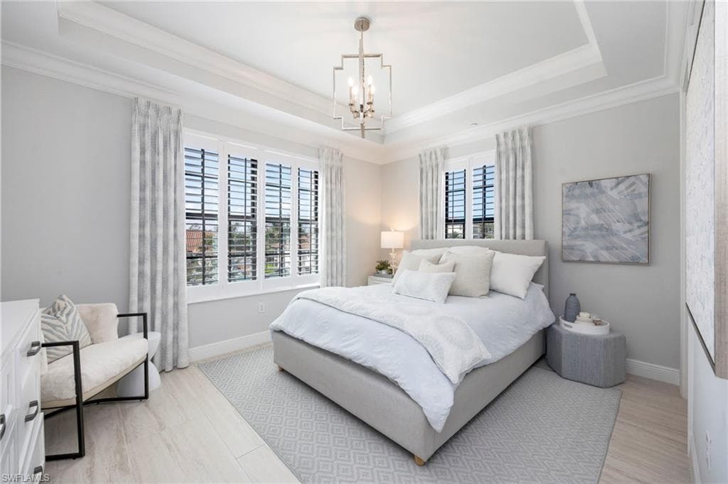 Bedroom with suspended lighting, a raised ceiling, and light wood-style flooring