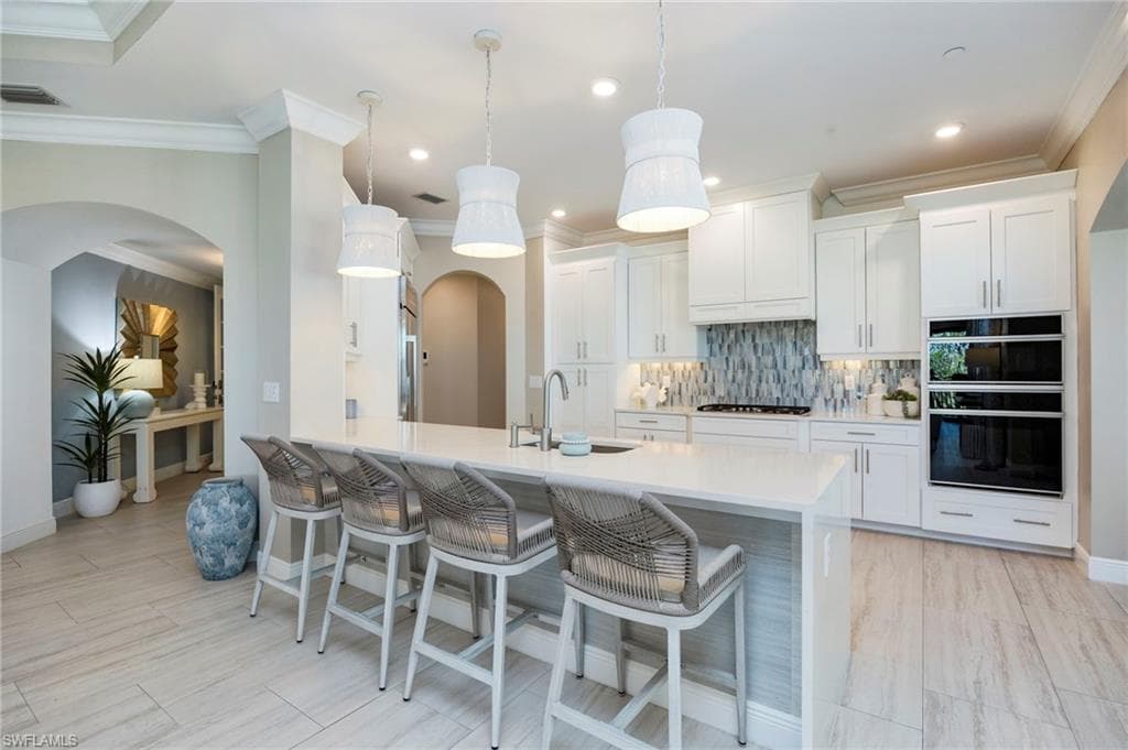 Kitchen with a breakfast bar, arched walkways, white cabinets, tasteful backsplash, and a peninsula