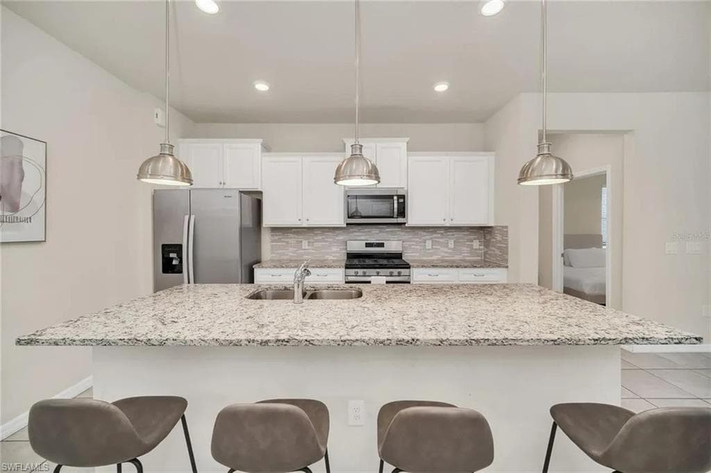 Kitchen with stainless steel appliances, a breakfast bar, white cabinets, and a center island with sink