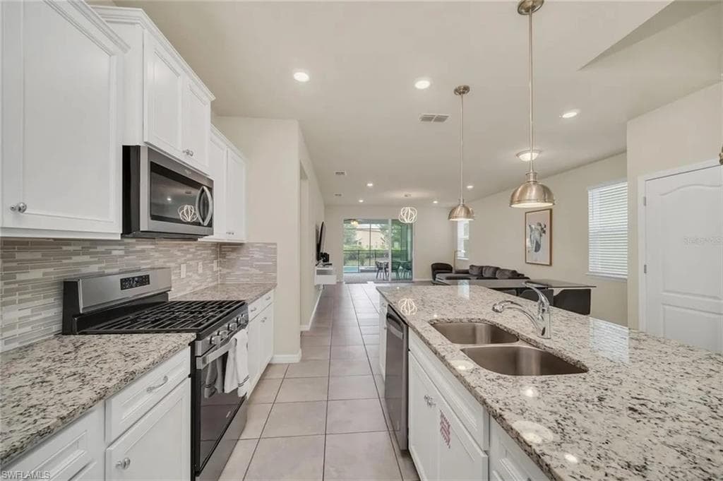 Kitchen with stainless steel appliances, white cabinets, light stone countertops, light tile patterned floors, and decorative light fixtures
