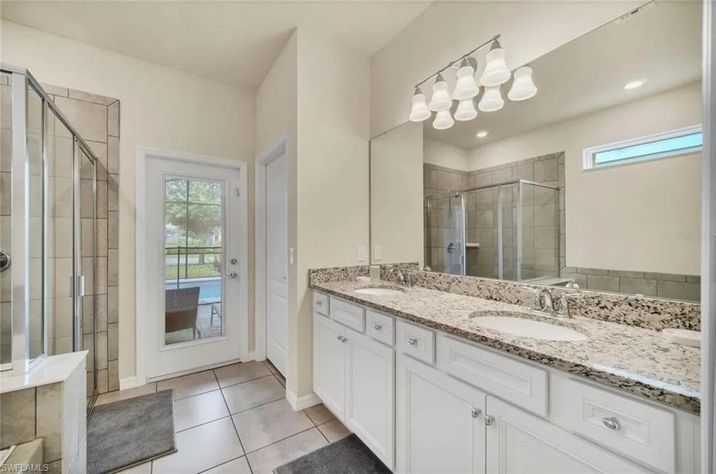 Full bathroom with double vanity, healthy amount of natural light, a shower stall, and light tile patterned floors