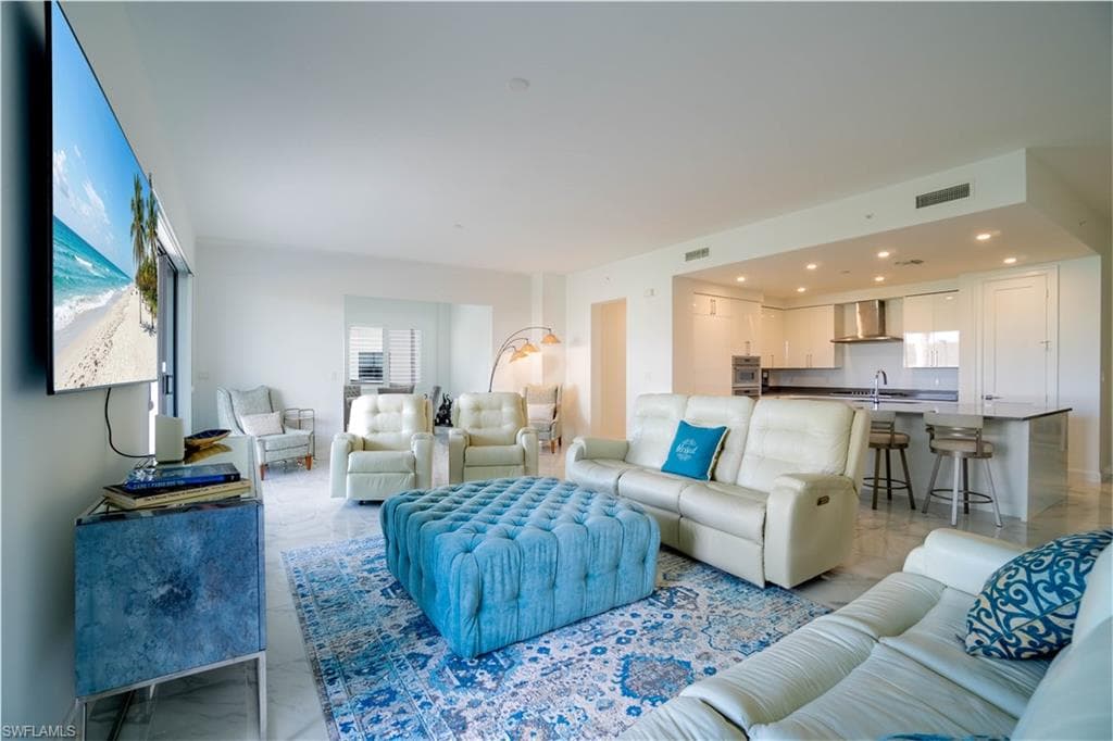 Bright open-concept living area featuring a kitchen with a peninsula island, white cabinetry, and stainless steel appliances