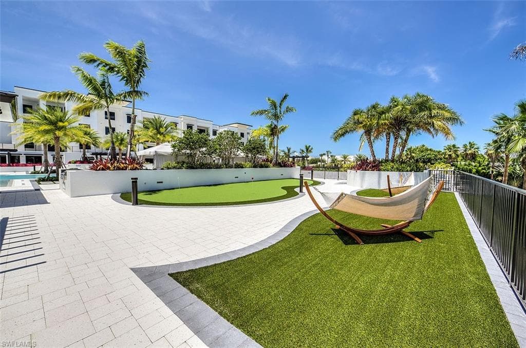 Outdoor amenity space featuring paver stone hardscaping, artificial turf lawn, and mature palm trees