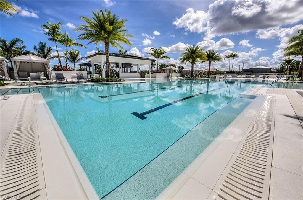 Resort-style pool area featuring a lap lane, surrounding lounge areas, a poolside cabana with seating, and tropical palm tree landscaping