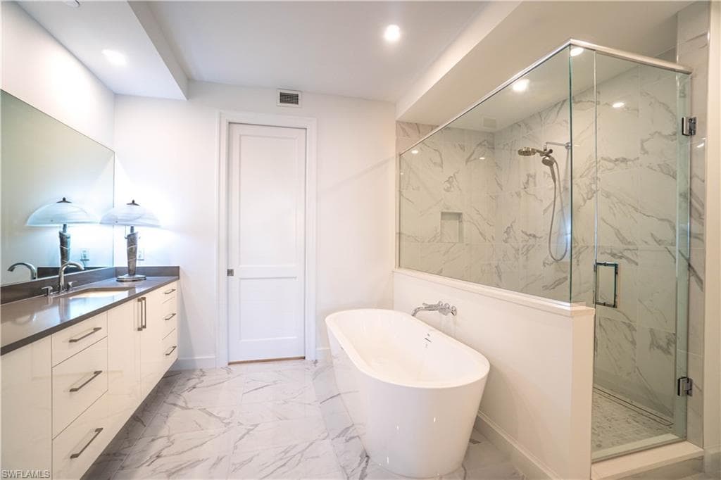 Full bathroom featuring a marble finish shower, light marble finish flooring, a freestanding tub, vanity, and recessed lighting