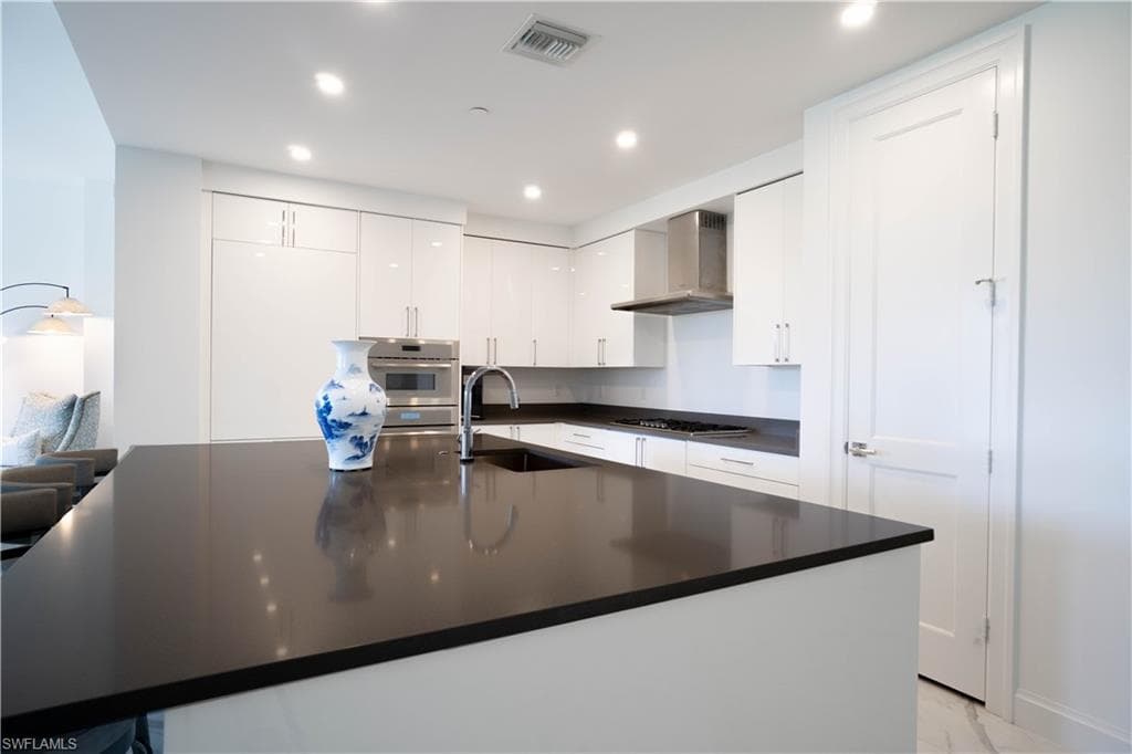 Contemporary kitchen featuring a spacious island with a dark countertop, white high-gloss cabinetry, and stainless steel appliances including a built-in microwave and range hood