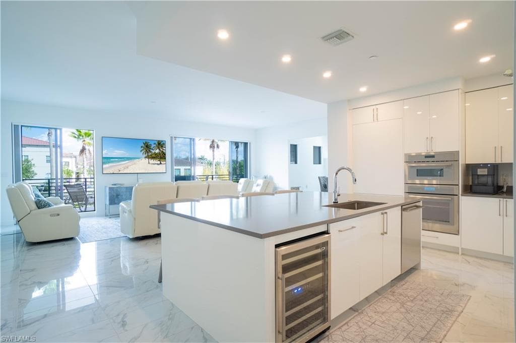 Kitchen featuring open floor plan, white cabinets, an island with sink, beverage cooler, and recessed lighting