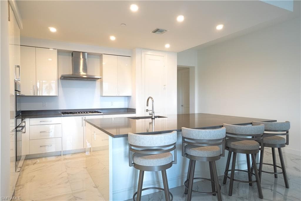 Kitchen with modern cabinets, recessed lighting, white cabinets, and light marble finish flooring