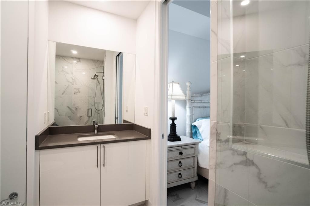 Ensuite bathroom featuring vanity, a marble finish shower, and marble look tiles
