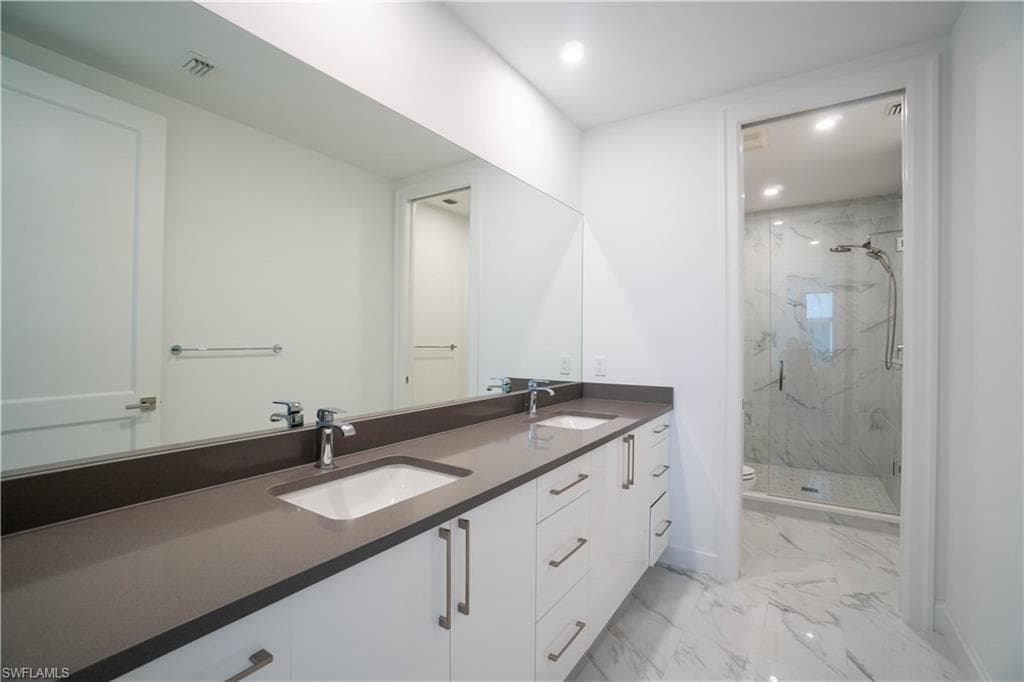 Bathroom with double vanity, a marble finish shower, light marble finish floors, and recessed lighting