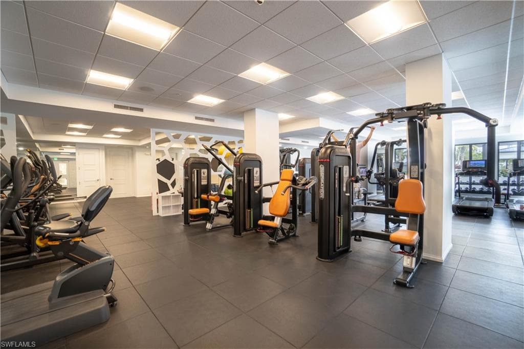 Fitness center with rubberized flooring, abundant overhead lighting, mirrored walls, and a variety of exercise equipment including cardio machines and weight stations