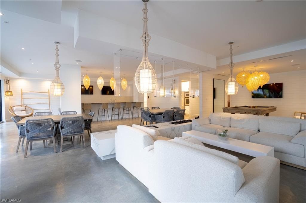 Spacious entertainment area featuring concrete flooring, a built-in wet bar with seating, multiple pendant light fixtures, and a shiplap accent wall