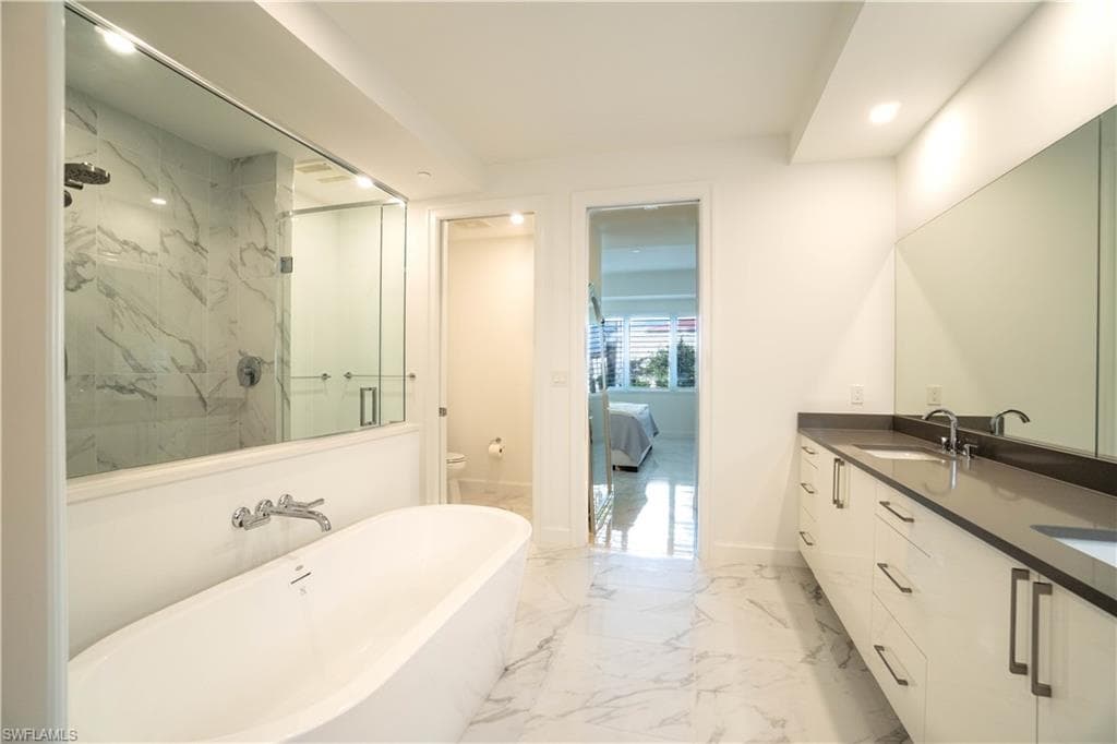 Ensuite bathroom with double vanity, a marble finish shower, light marble finish flooring, recessed lighting, and a freestanding tub