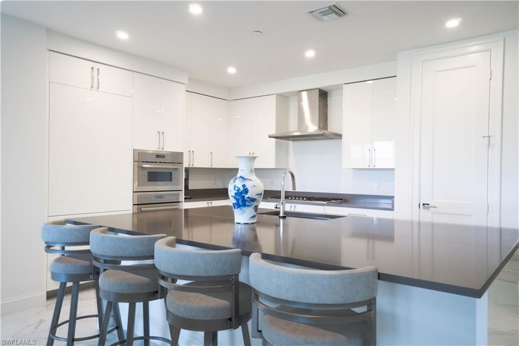Contemporary kitchen featuring a large central island with seating, high-gloss white cabinetry, stainless steel appliances, and recessed lighting