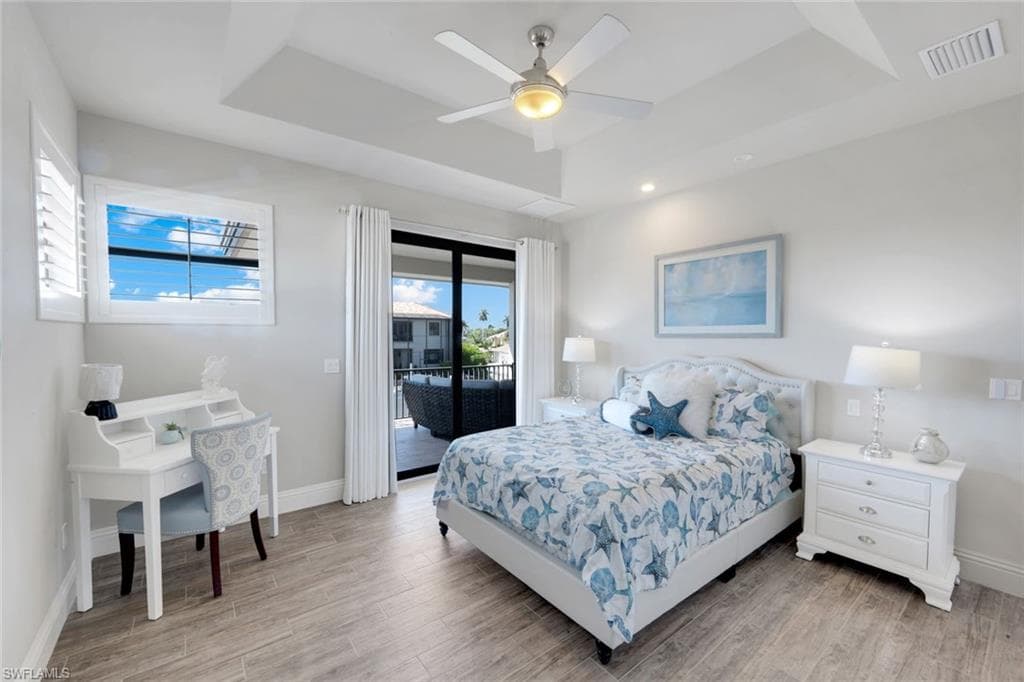 Bedroom featuring a raised ceiling, light wood-style floors, access to exterior, and ceiling fan