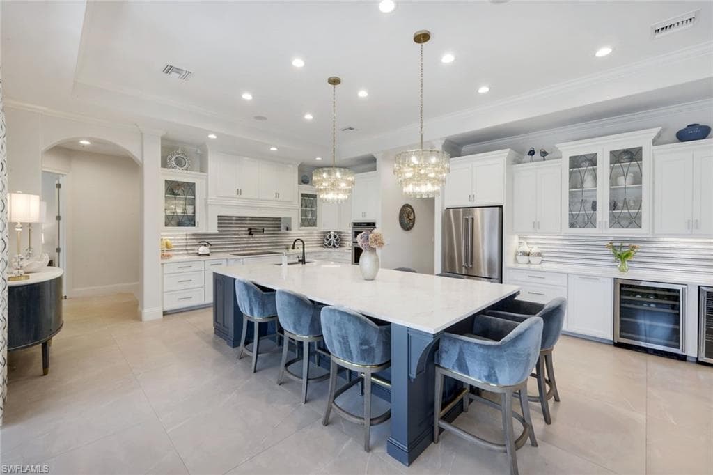 Two tone kitchen with glass fronted cabinets, decorative backsplash, a breakfast bar area, arched walkways, and ornamental molding