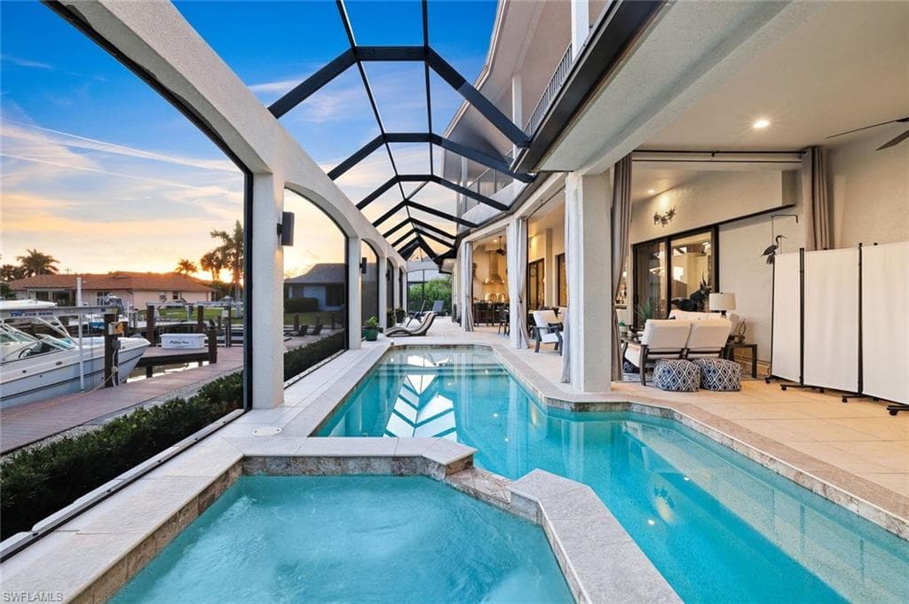 Pool at dusk with a sunroom, a patio, a pool with connected hot tub, glass enclosure, and an outdoor lounge area