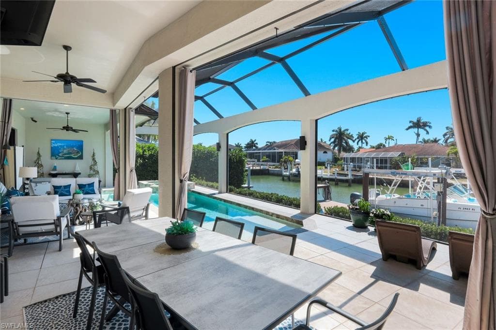 View of patio / terrace featuring outdoor dining space, glass enclosure, ceiling fan, a water view, and a sunroom