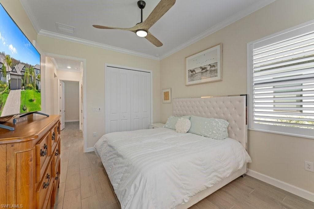 Bedroom featuring light wood finished floors, crown molding, ceiling fan, a closet, and multiple windows