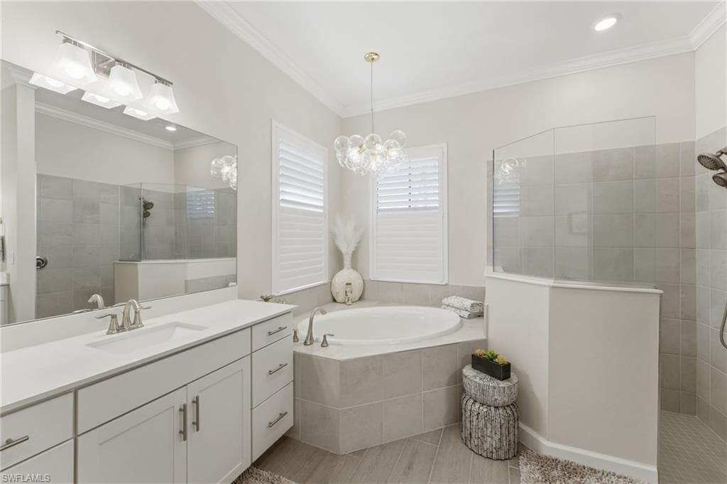 Full bath with a walk in shower, vanity, ornamental molding, a bath, and suspended lighting