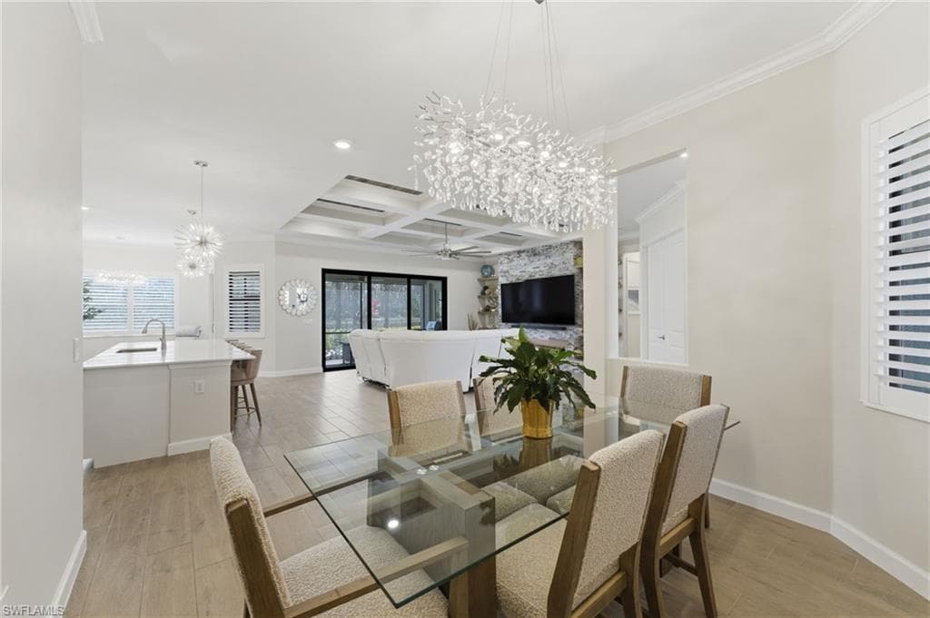 Dining area featuring suspended lighting, light wood-type flooring, coffered ceiling, a ceiling fan, and ornamental molding