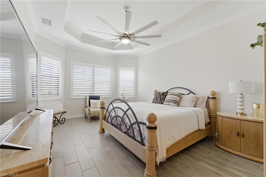 Bedroom with wood finish floors, a ceiling fan, crown molding, and a tray ceiling