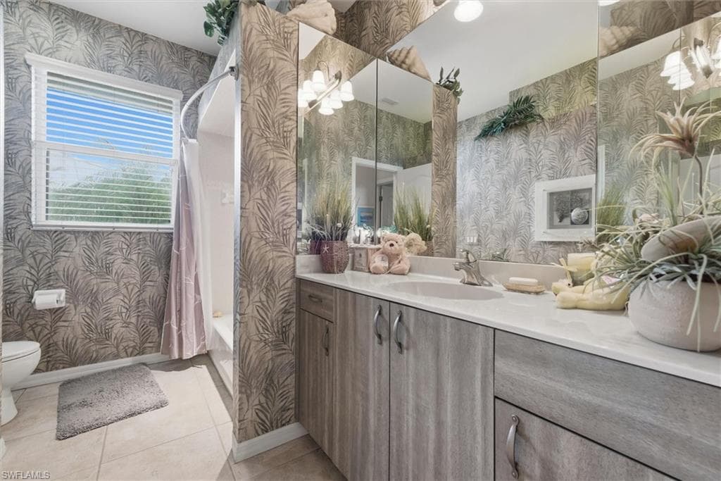 Full bathroom with wallpapered walls, vanity, light tile patterned floors, and shower / bathtub combination with curtain