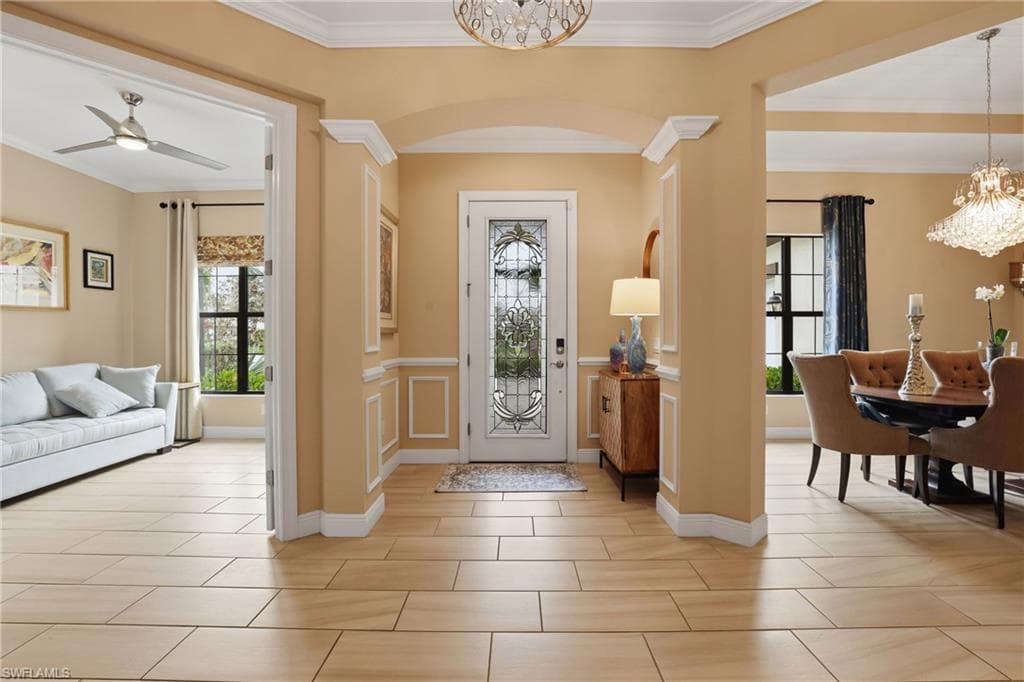 Foyer entrance featuring suspended lighting, crown molding, a wainscoted wall, ceiling fan, and arched walkways