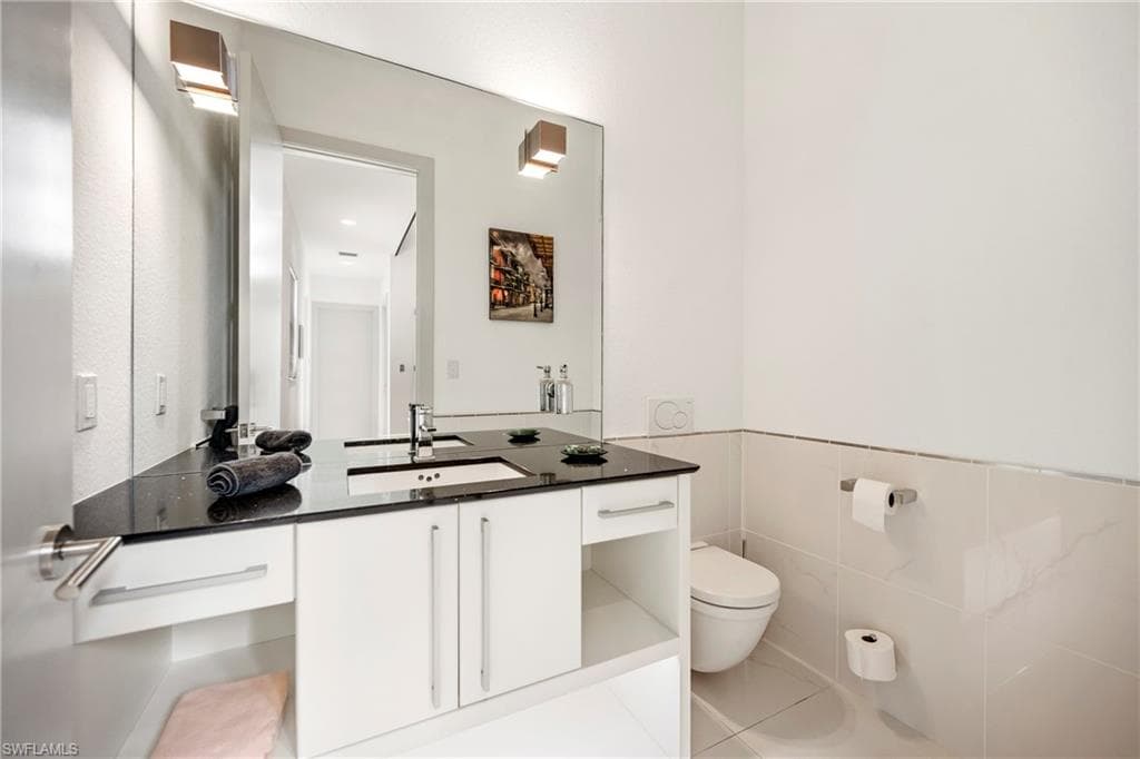 half bathroom featuring vanity, tile walls, light tile patterned floors, and a wainscoted wall
