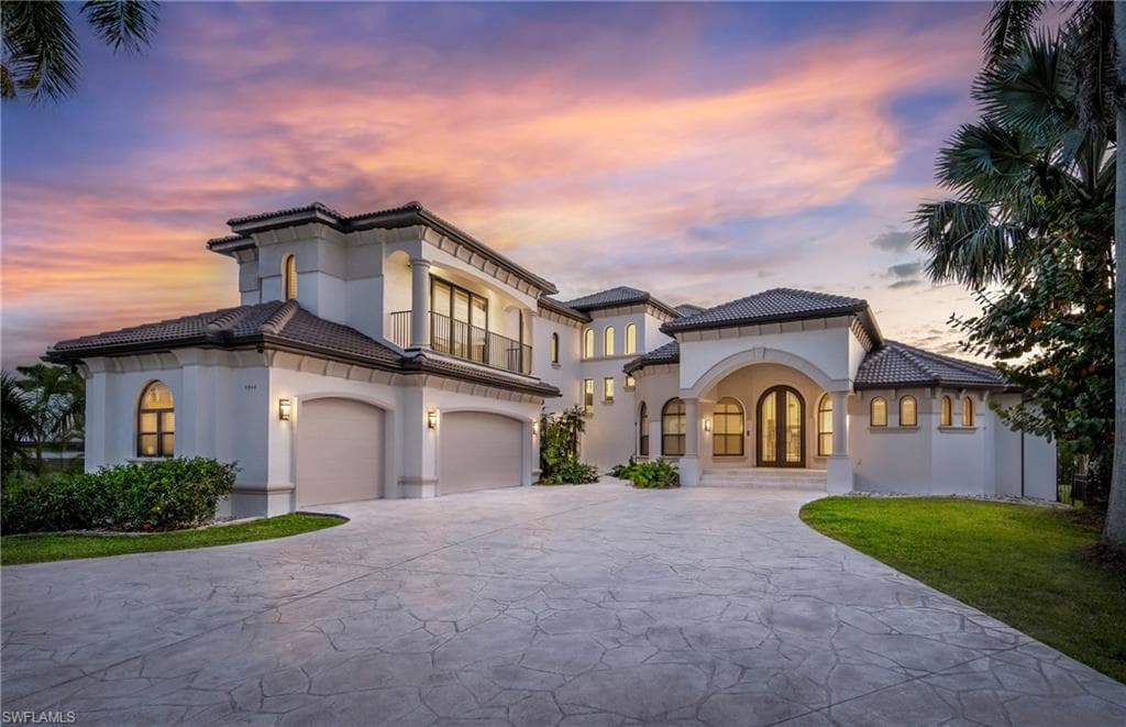 Mediterranean / spanish house with french doors, concrete driveway, stucco siding, a balcony, and a tile roof