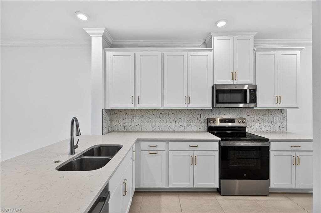 Kitchen with stainless steel appliances, white cabinetry, light stone counters, crown molding, and decorative backsplash