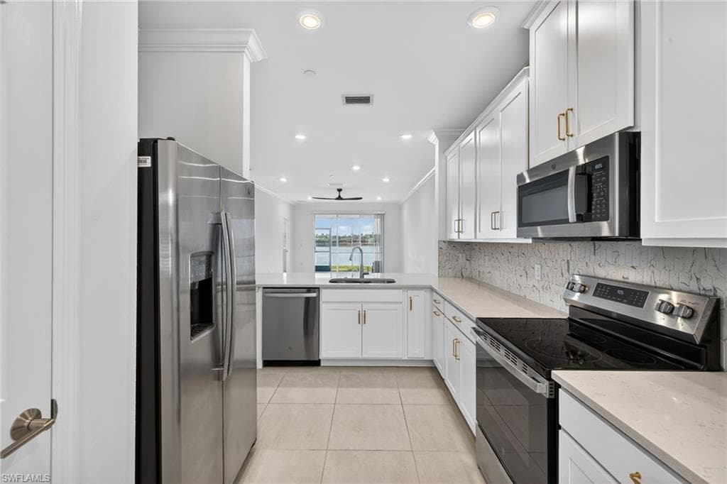Kitchen featuring stainless steel appliances, white cabinetry, recessed lighting, light tile patterned flooring, and light stone counters