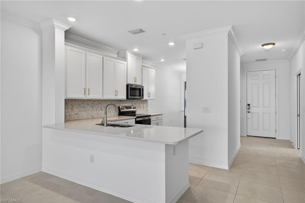 Kitchen featuring a peninsula, stainless steel appliances, decorative backsplash, white cabinets, and light stone counters