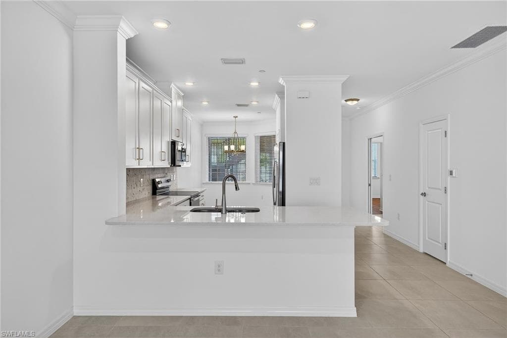 Kitchen featuring light stone countertops, a peninsula, crown molding, white cabinets, and stainless steel appliances