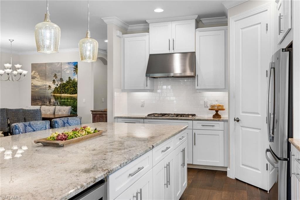 Kitchen with light stone counters, white cabinetry, crown molding, dark wood-style flooring, and freestanding refrigerator