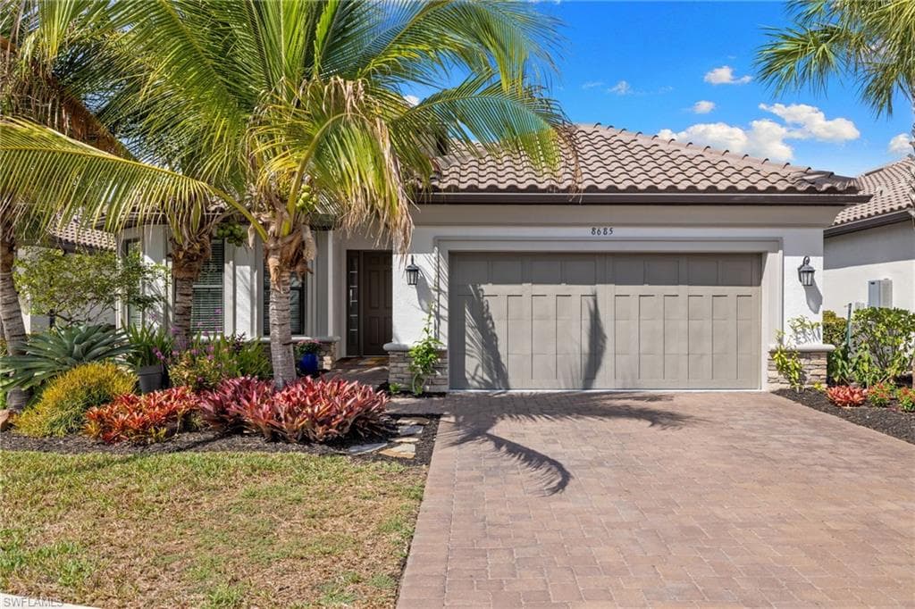 View of front facade with decorative driveway, stucco siding, an attached garage, and a tile roof