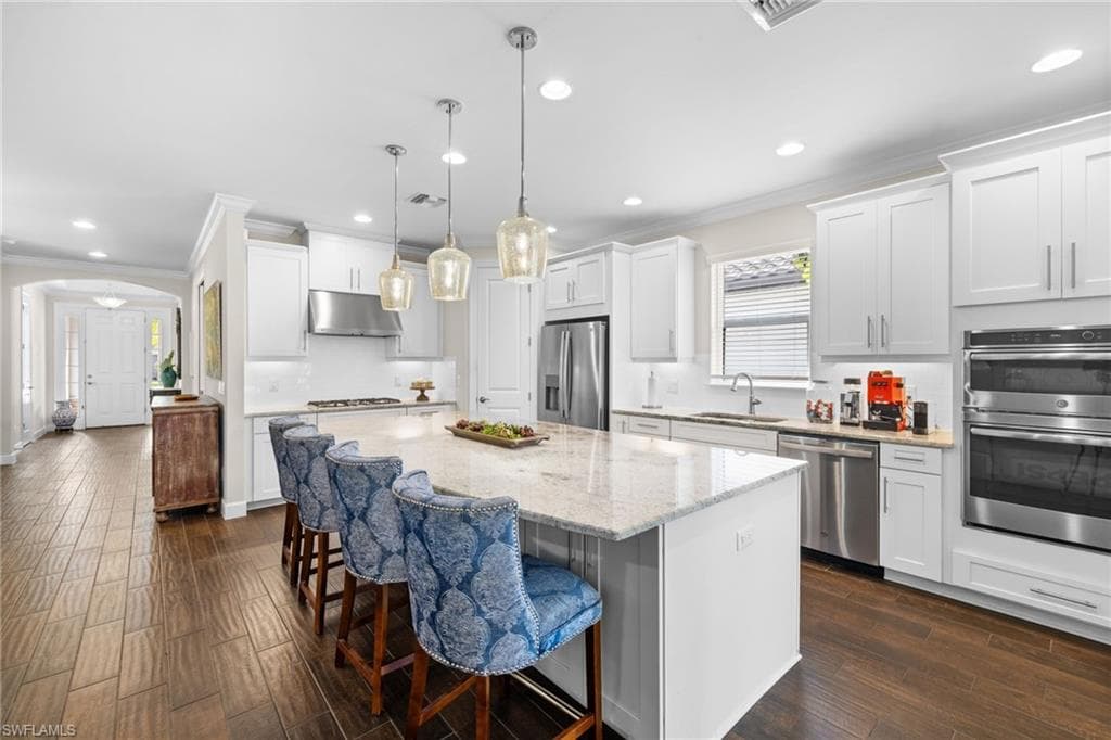 Kitchen featuring backsplash, arched walkways, a kitchen bar, crown molding, and white cabinetry
