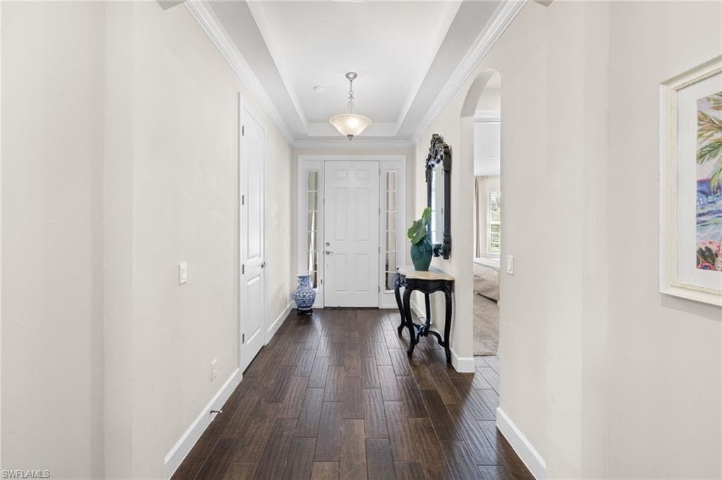 Foyer entrance featuring a raised ceiling, arched walkways, and dark wood finished floors