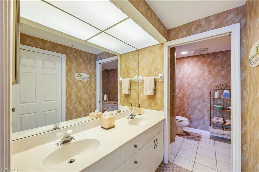 Bathroom with wallpapered walls, double vanity, and light tile patterned floors