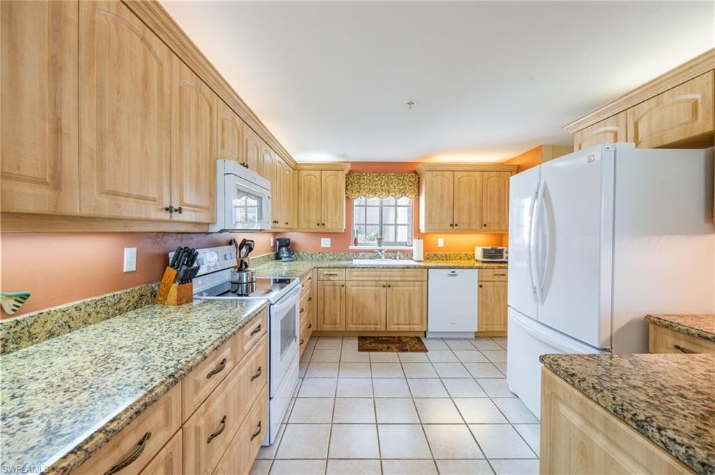 Kitchen with light wood finish cabinets, white appliances, light stone counters, and light tile patterned flooring