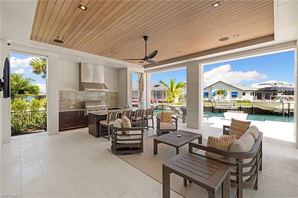 View of patio / terrace featuring an outdoor kitchen and area to lounge, ceiling fan, a water view, an outdoor pool, and a residential view