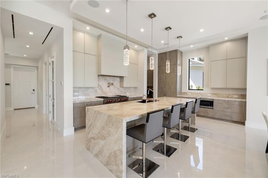 Dual tone kitchen featuring modern cabinets, light stone counters, dual tone cabinetry, an island with sink, and pendant lighting