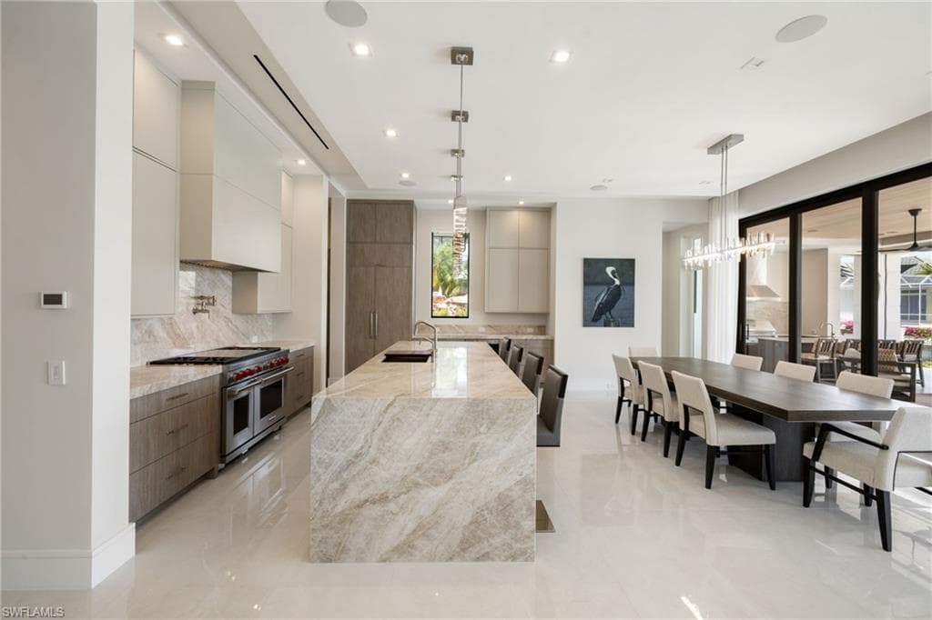 Two tone kitchen with light stone counters, modern cabinets, two tone cabinets, double oven range, and a large island with sink