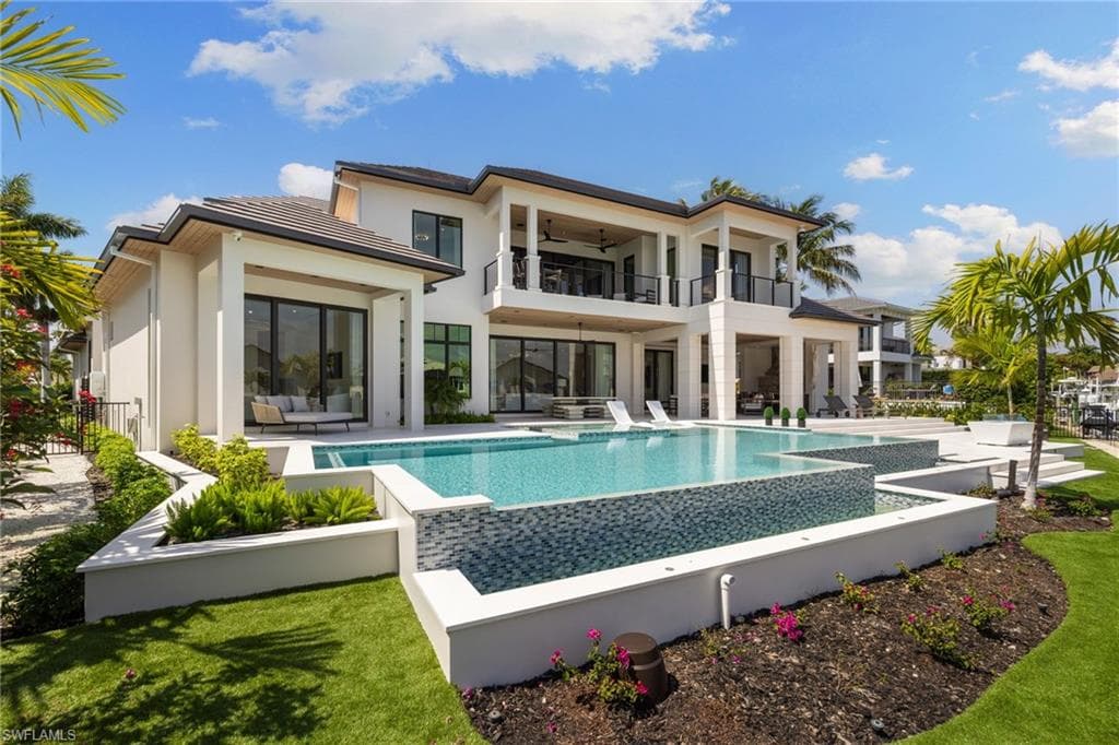 Rear view of house with an infinity pool, a patio area, ceiling fan, and a balcony